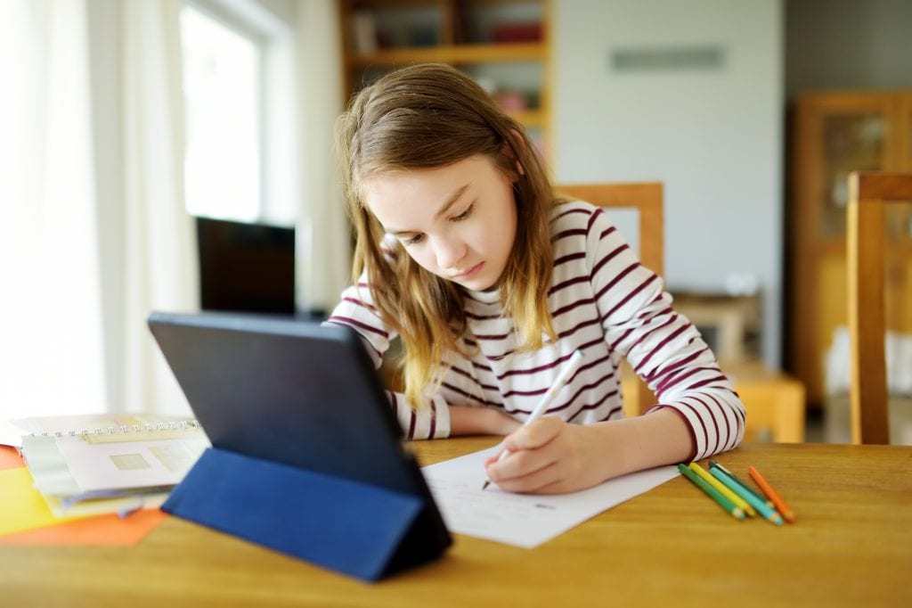 Smart preteen schoolgirl doing her homework with digital tablet at home. Education and distance learning for kids. Homeschooling during quarantine.